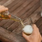 Man pouring beer in glass on a wooden picnic table