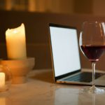 Glass of sweet red wine with candles and laptop in the background.