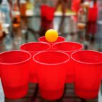 6 red beer pong cups with an orange ping pong ball sitting on top surrounded by alcohol. Saucey.