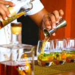 man pouring rum into 3 glasses full of liquor