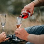 Couple laying in a field drinking wine out of clear wine glasses