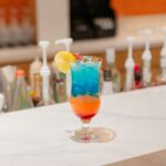 Colorful layered cocktail with a lemon slice on a bar